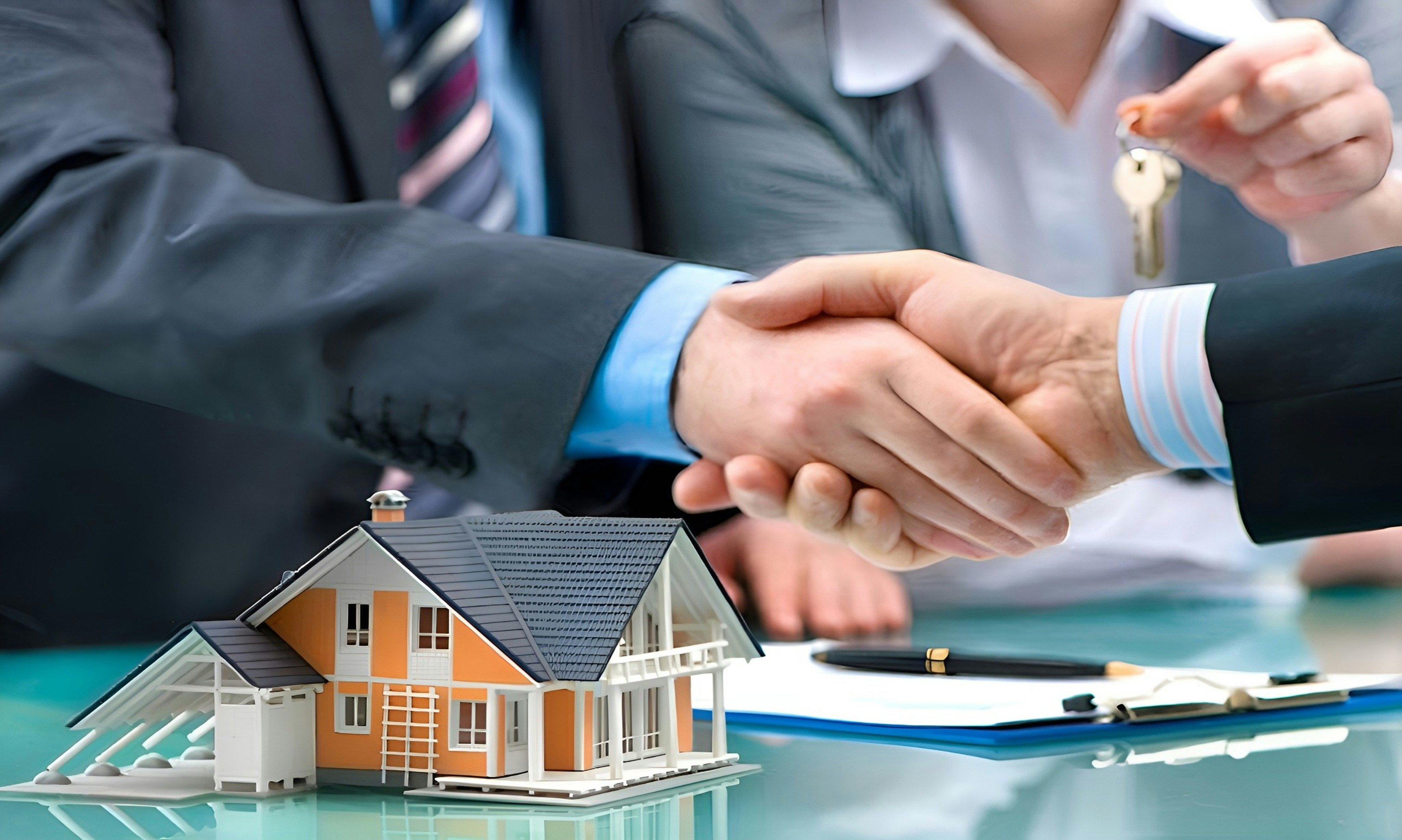 A professional shaking hands with clients over a house model and keys